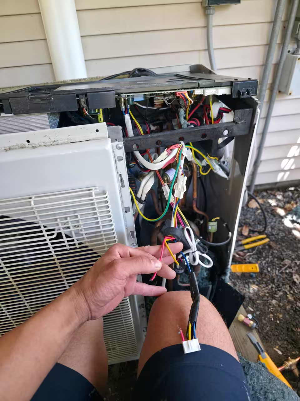 Electrical repair being completed inside an outdoor AC condenser